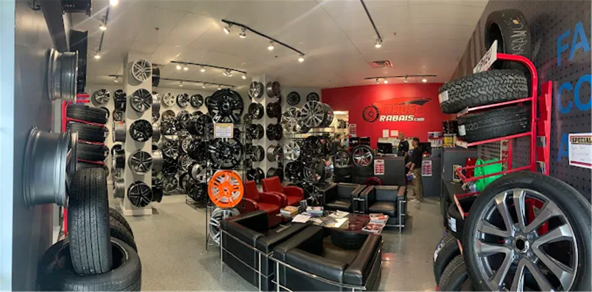 Wide %STORENAME% showroom with wheel displays, tire racks, seating, and branded service wall.