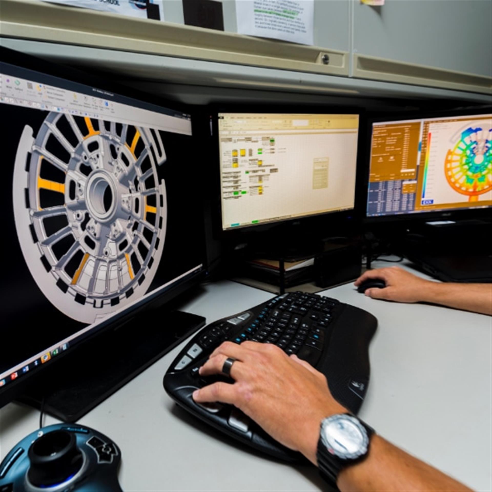 Automotive engineer working at a multi-monitor workstation displaying a detailed wheel design and engineering software.